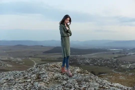 Молодая женщина в пальто стоит на скале над долиной