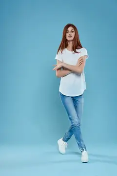 Рыжеволосая девушка в белой футболке и джинсах на голубом фоне