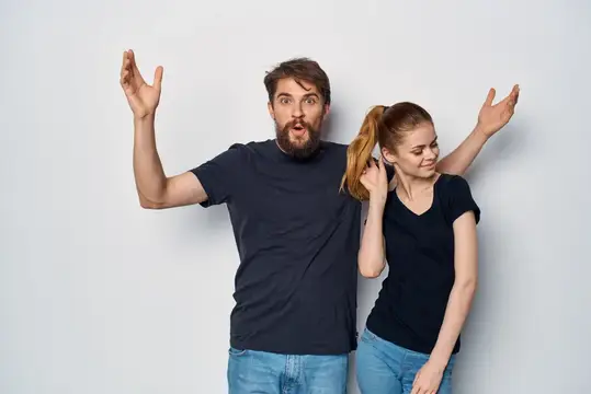 Удивлённый мужчина с бородой и улыбающаяся девушка с хвостиком на сером фоне