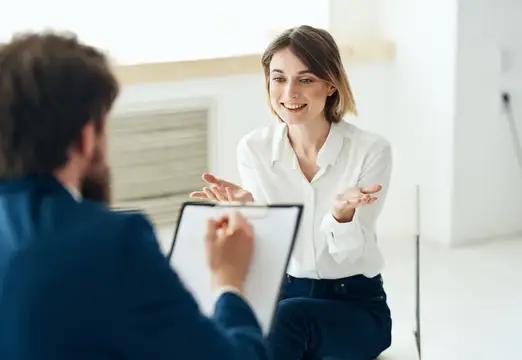 Улыбающаяся женщина на собеседовании отвечает мужчине с планшетом