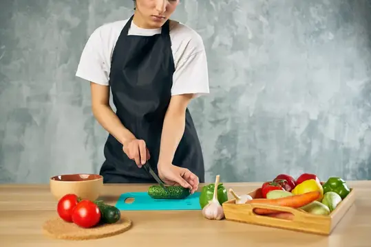 Молодая женщина в фартуке режет огурец на кухне