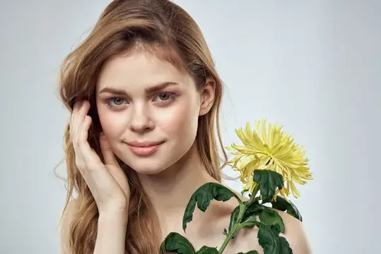 Молодая светловолосая женщина с жёлтой хризантемой на сером фоне
