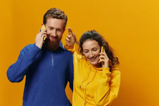 Мужчина и женщина весело разговаривают по телефонам на жёлтом фоне