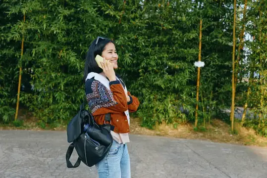 Улыбающаяся азиатская девушка говорит по телефону на фоне бамбука