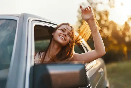 Счастливая девушка высунулась из окна машины на закате