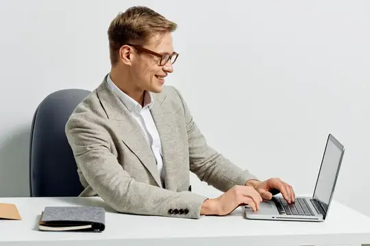 Улыбающийся мужчина в очках работает за ноутбуком в офисе