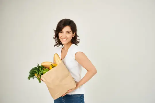 Улыбающаяся брюнетка с бумажным пакетом продуктов на светлом фоне