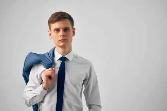Молодой мужчина в рубашке с галстуком держит пиджак на плече