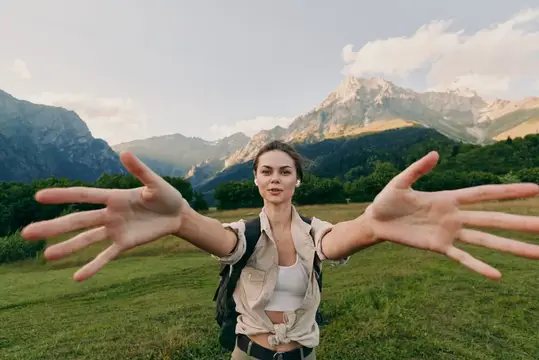 Девушка с рюкзаком раскинула руки на фоне гор