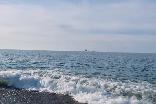 Волна прибоя на галечном пляже и сухогруз в море