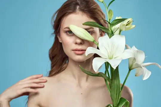 На фотографии высокого качества изображена красивая женщина с обнаженными плечами, украшенными цветами, на фоне чистого голубого фона