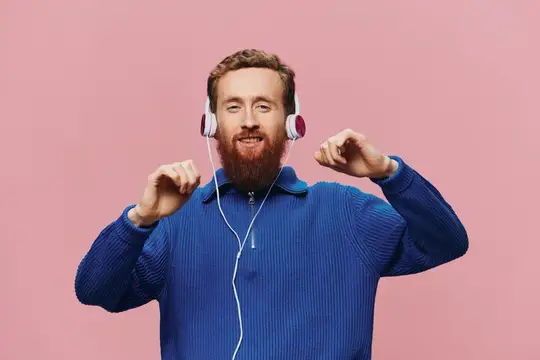 Рыжебородый мужчина в наушниках танцует на розовом фоне
