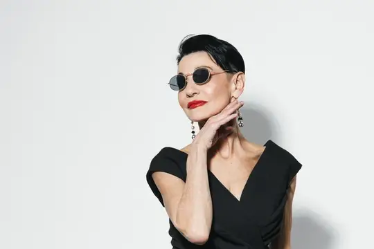 Элегантная женщина в солнцезащитных очках и черном платье на белом фоне