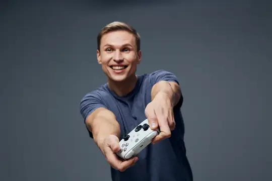 Улыбающийся парень протягивает игровой контроллер на сером фоне