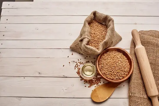Пшеничные зёрна в мешке и миске на светлом деревянном столе