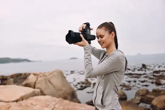 Молодая девушка фотографирует пейзаж на камеру у моря