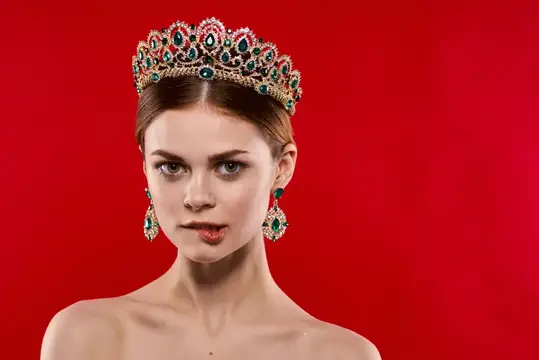 Молодая женщина в роскошной короне с изумрудами на красном фоне