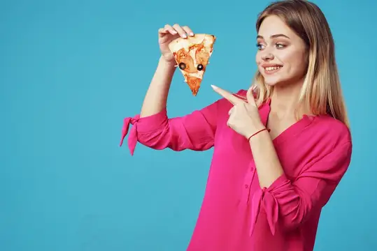 Улыбающаяся блондинка в розовой блузке указывает на кусок пиццы