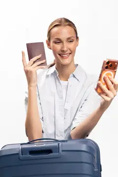Улыбающаяся светловолосая женщина с паспортом и смартфоном у чемодана