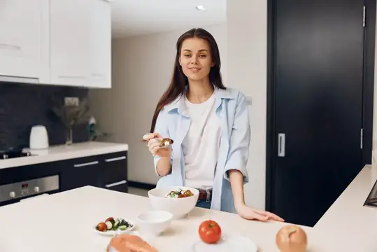 Молодая женщина ест салат на светлой кухне