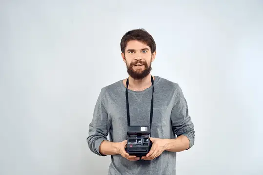 Бородатый мужчина с ретро-фотоаппаратом на сером фоне