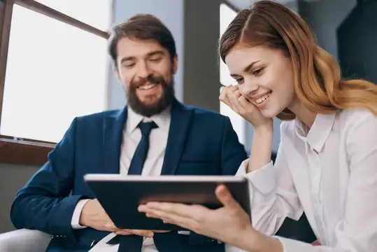 Улыбающиеся коллеги рассматривают планшет в офисе