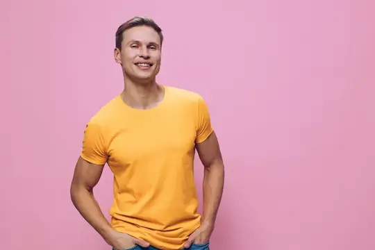 Улыбающийся мужчина в желтой футболке стоит на розовом фоне, демонстрируя повседневный стиль и уверенное выражение лица, молодой человек европеоидной расы, воплощающий образ жизни цифрового…