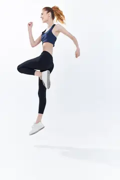 Рыжеволосая девушка в спортивной форме прыгает с высоко поднятым коленом