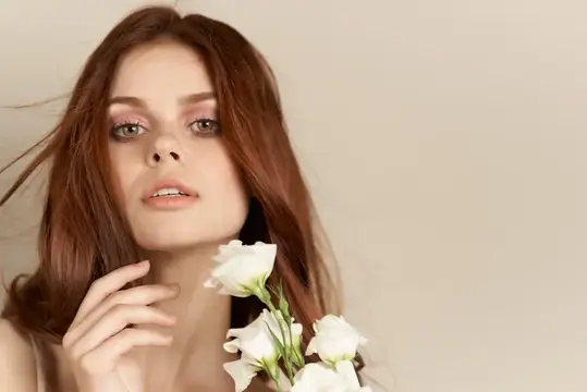 Рыжеволосая девушка с белыми цветами у лица на бежевом фоне