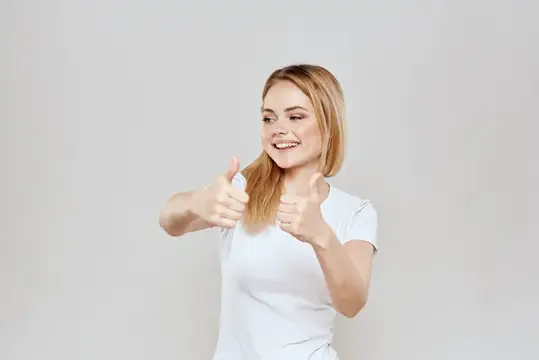 Улыбающаяся блондинка в белой футболке показывает два больших пальца вверх