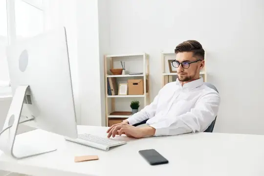 Молодой мужчина в очках работает за компьютером в светлом офисе