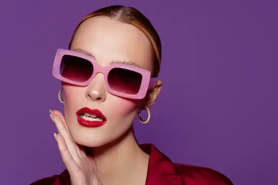 Молодая женщина в розовых солнцезащитных очках на фиолетовом фоне