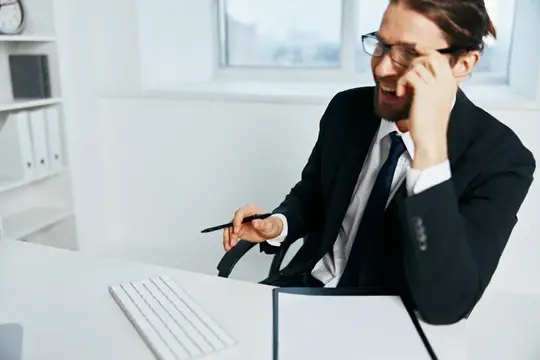 Улыбающийся бородатый мужчина в очках говорит по телефону в офисе