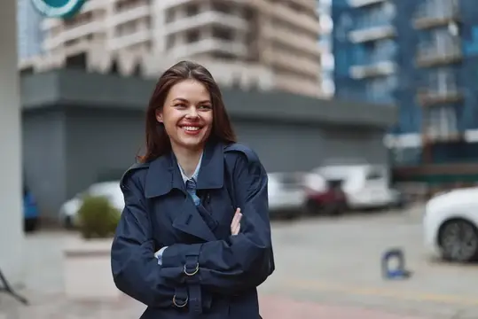Улыбающаяся темноволосая девушка в синем плаще на городской улице