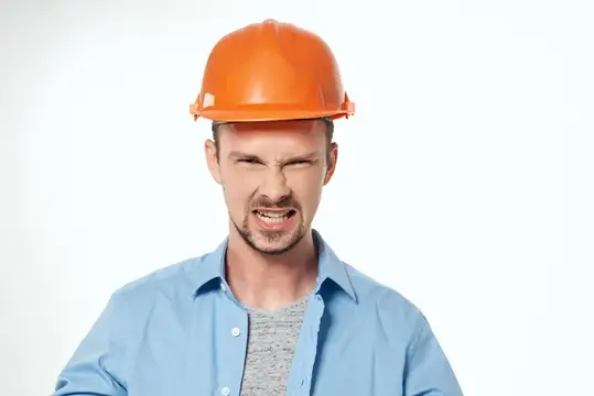 Молодой мужчина в оранжевой каске кривится от напряжения