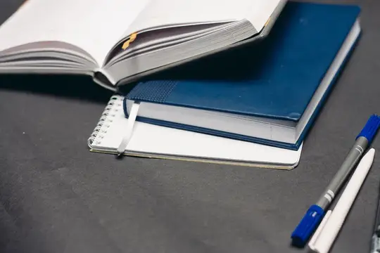 На сером фоне на рабочем столе лежат блокнот и ручка для офисной работы