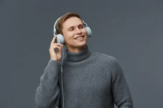 Улыбающийся парень в наушниках слушает музыку на сером фоне
