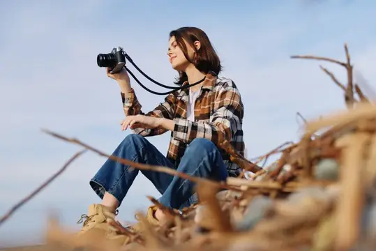 Девушка с фотокамерой сидит на сухой траве под ясным небом