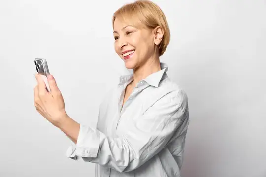 Улыбающаяся блондинка в белой рубашке смотрит в смартфон