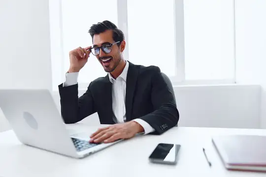 Улыбающийся бородатый мужчина в очках работает за ноутбуком в офисе