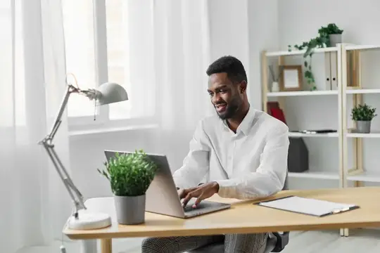 Улыбающийся темнокожий мужчина работает за ноутбуком в светлом офисе