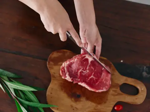 Женщина с ножом в руке нарезает свежее стейковое мясо для запекания на кухне