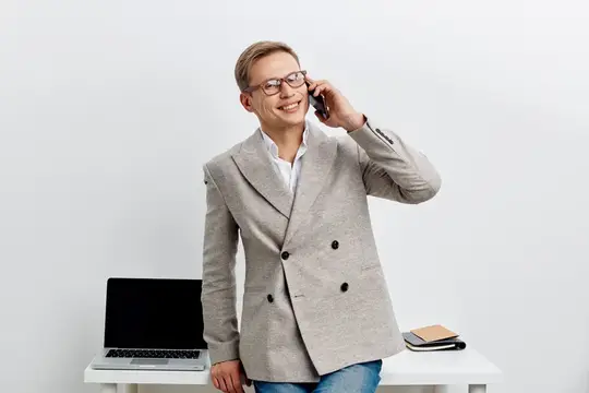Улыбающийся мужчина в очках говорит по телефону у стола с ноутбуком