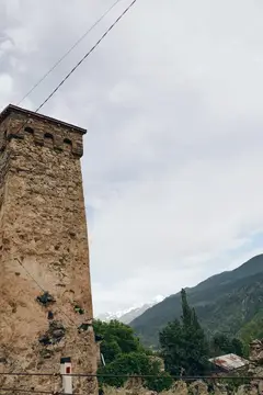 Старинная каменная башня на фоне гор и пасмурного неба