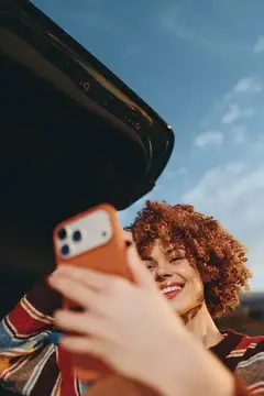 Рыжеволосая девушка с кудрями делает селфи на смартфон на улице