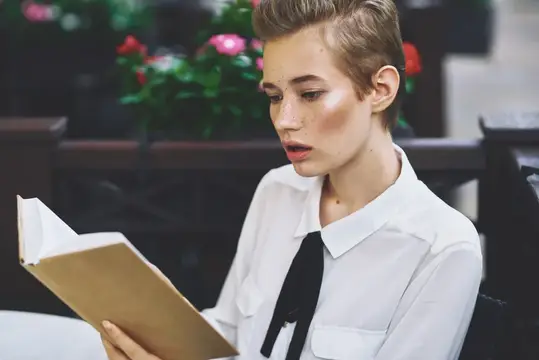 Молодая женщина с короткой стрижкой читает книгу в белой рубашке