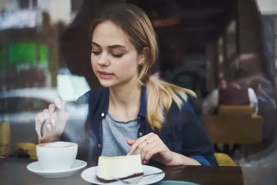 Молодая блондинка с кофе и куском торта в кафе