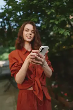 Молодая женщина в красной рубашке смотрит в смартфон на улице