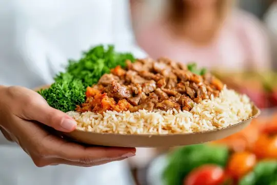 Руки держат тарелку с рисом, мясом и зеленью