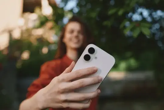 Улыбающаяся девушка держит белый смартфон на фоне зелени
